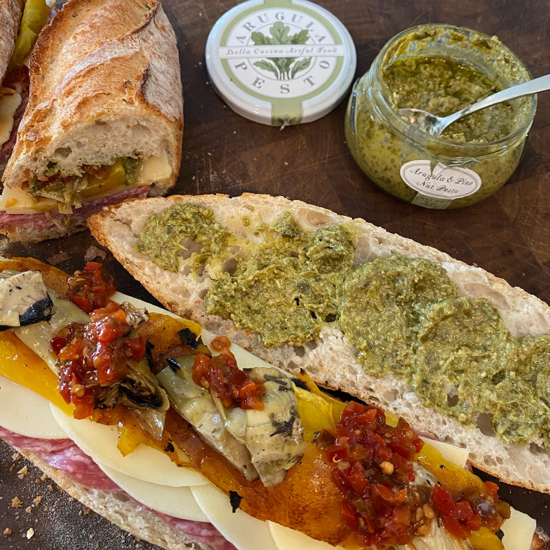 bella cucina pesto featured in garden gift box spred on french bread with peppers, cheese and salami on a cutting board