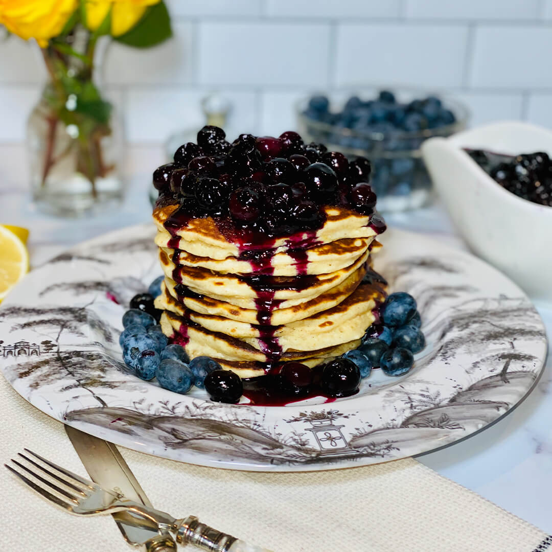 blueberry pancakes in a stack topped with blueberry sauce on a plate