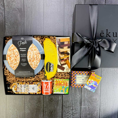 Gift box filled with games, popcorn, popcorn popper in a black box with a black bow. 