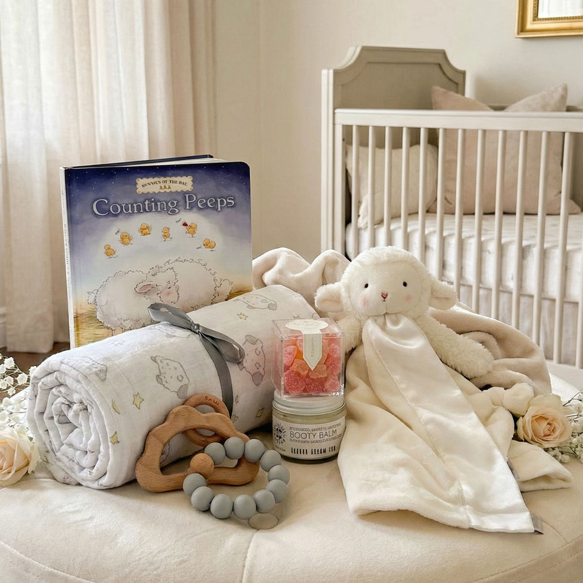 Modern gender-neutral baby lamb gift box with a plush toy, essentials, and Sugarfina champagne bubble gummies in a nursery setting.