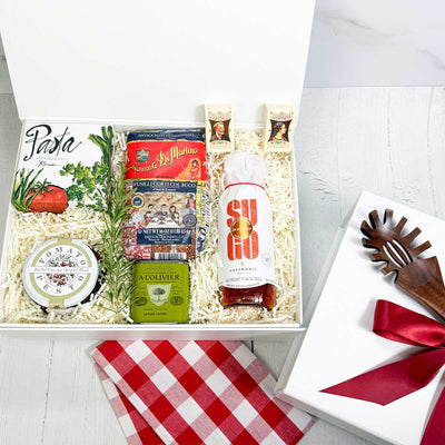ekuBOX gift box with Italian-themed products including pasta and olive oil, pasta sauce, dipping dishes on a white background. White box with pasta spoon and a red ribbon.