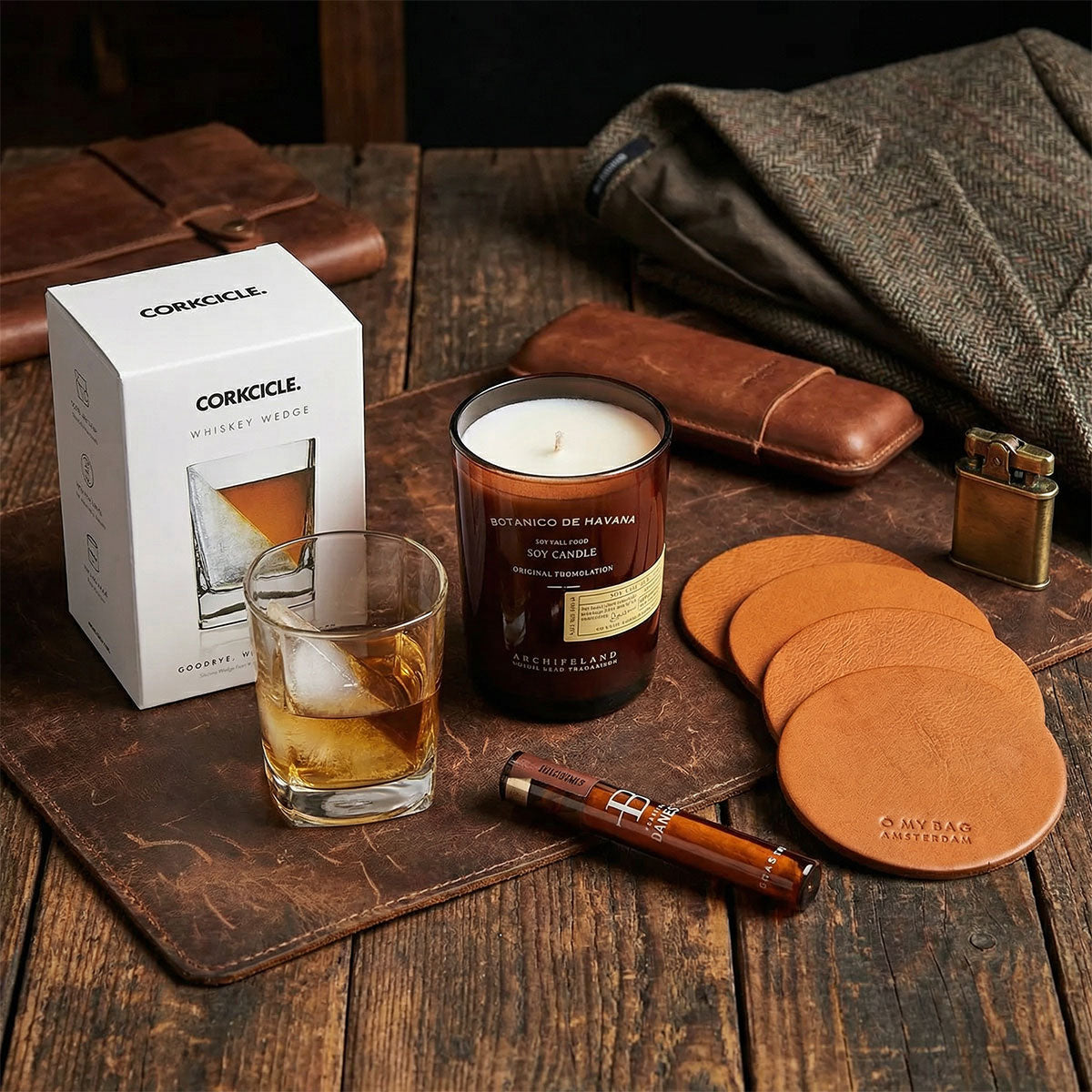 Candle, glass of whiskey, and other items on a wooden surface with a Corkcicle box.