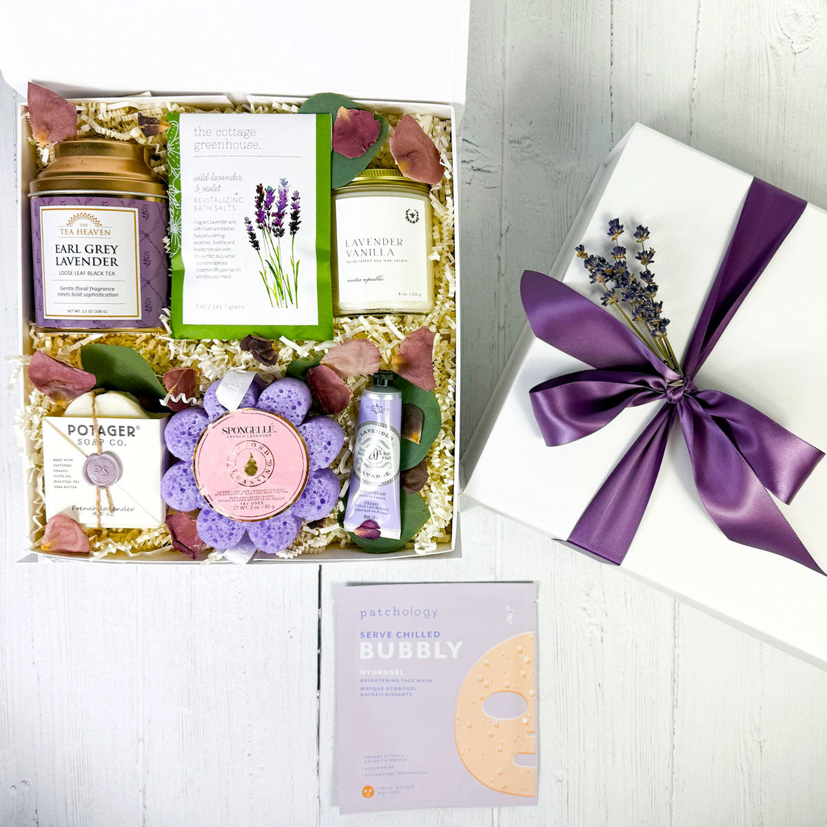 A top view of a gift box containing various lavender-infused spa products including a candle, hand cream, soap, bath salts, a body wash infused sponge, and tea. Relaxation gift box