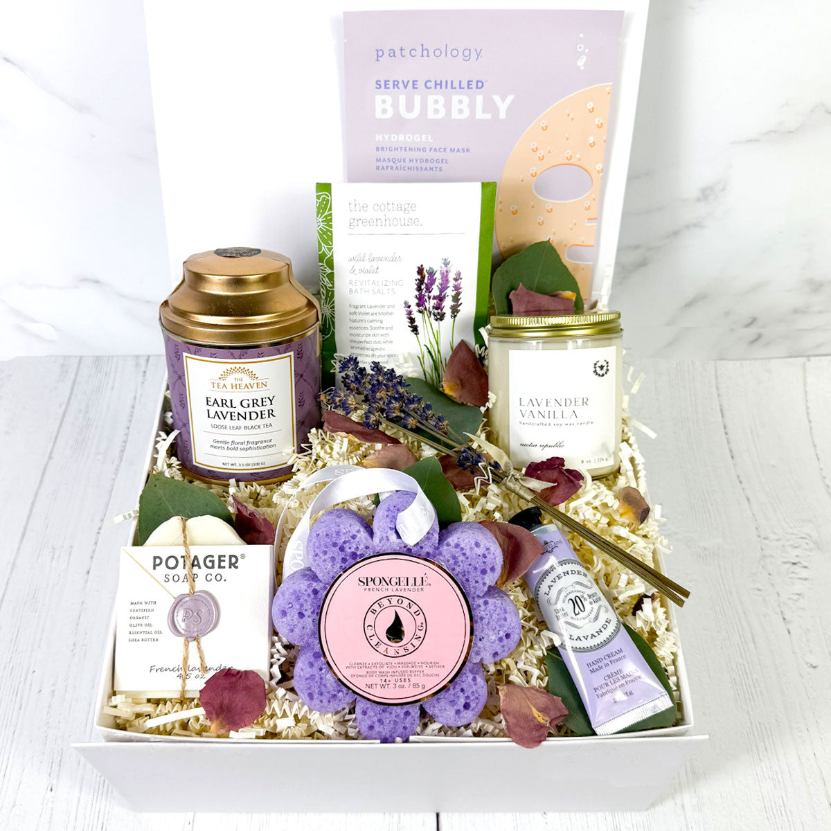 A gift box containing various lavender-infused spa products including a candle, hand cream, soap, bath salts, a body wash infused sponge, and tea. Relaxation gift box