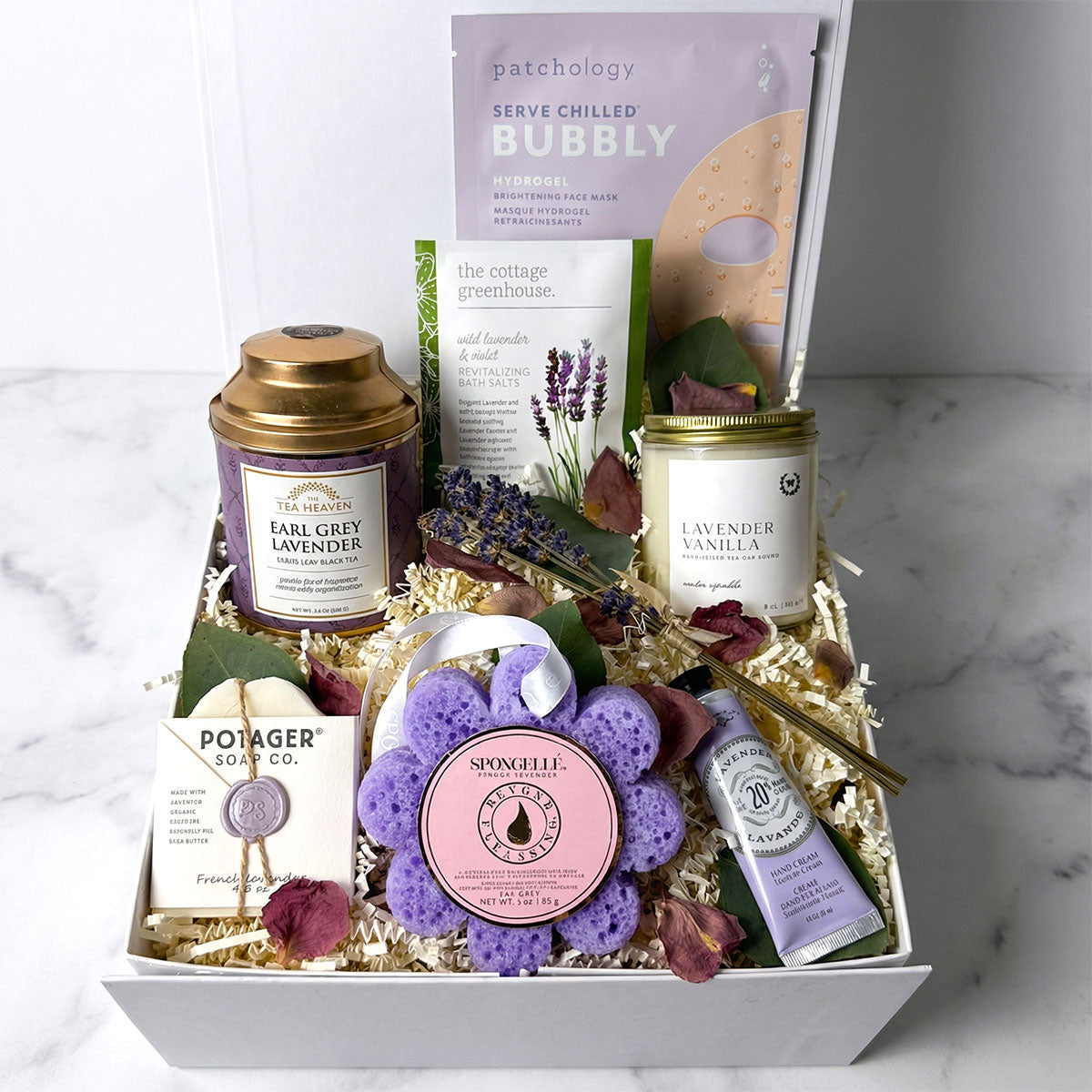 A gift box containing lavender-infused spa products including a candle, hand cream, soap, bath salts, a body wash infused sponge, and tea. Relaxation gift box