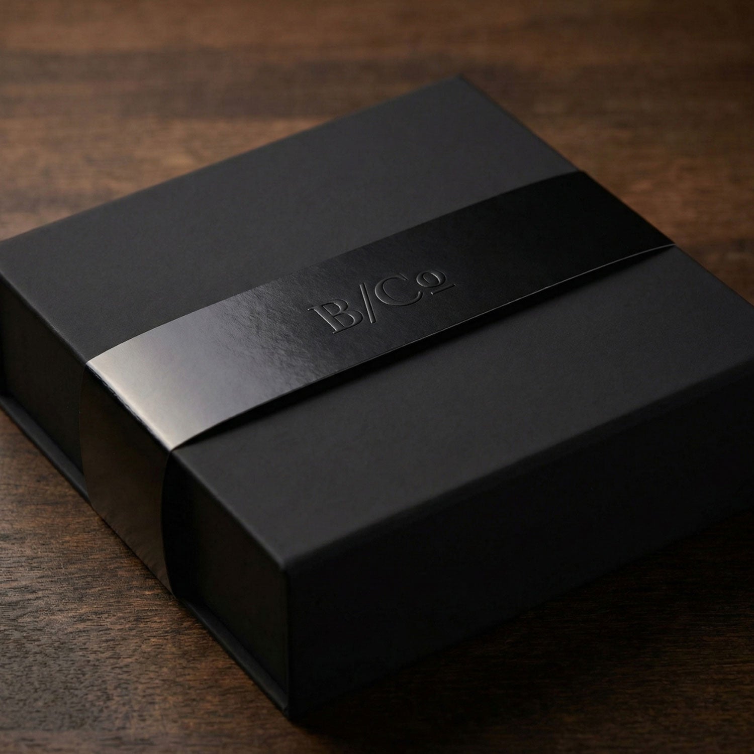 Semi-custom gifting service: black gift box with a belly band and an embossed logo on the wood surface.