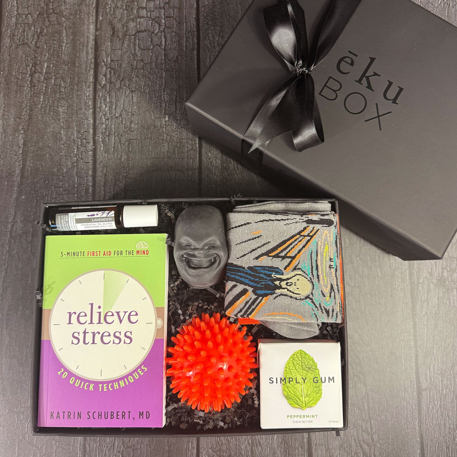 A gift box containing various items to relieve stress, including a stress ball, lavender oil roller, gum, a book, and a pair of socks .