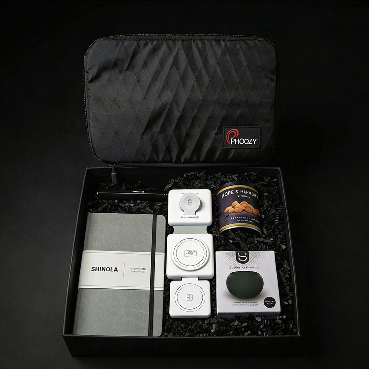 a tech gift box including a Shinola pen, notebook, a black NASA-tested tech bag, a 3 way charger, a mini speaker and a can of roasted peanuts.
