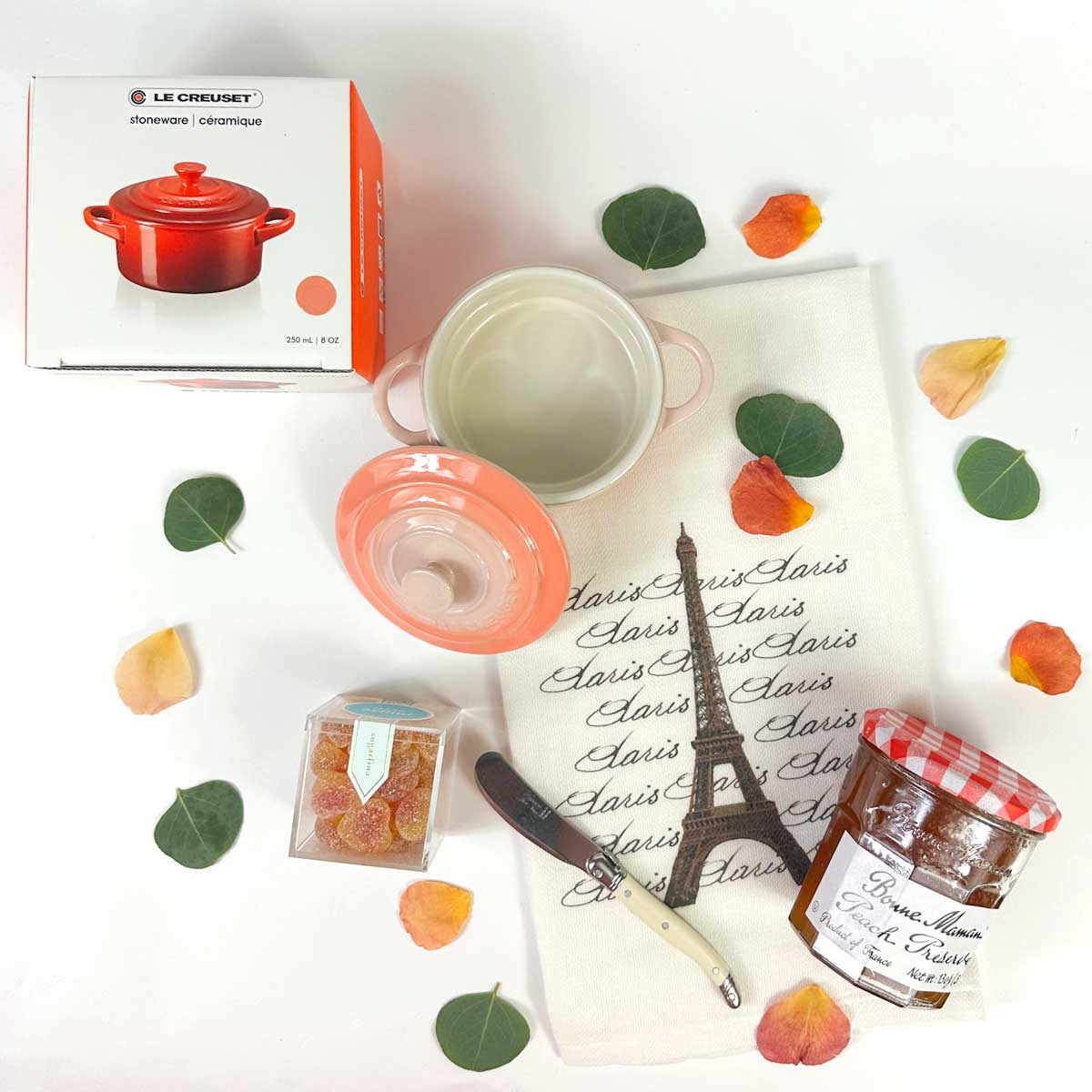  top view of Le Creuset French Peach gift set - with peach jam, sugarfina peach bellini gummys, kitchen towel and flower petals